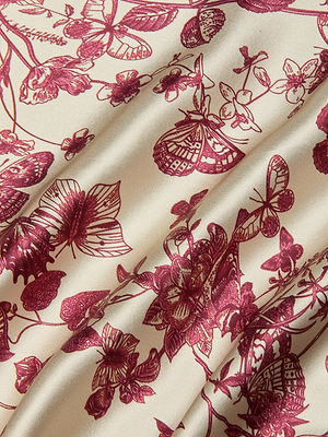 The Serita Silk Gown features cream-colored bias-cut silk charmeuse with a maroon floral butterfly print and detailed illustrations, gently draped for soft folds and elegant shadows.