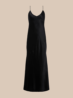 The Serita Silk Gown is a simple black slip dress with thin spaghetti straps and a subtly flared hem, shown against a plain beige background.