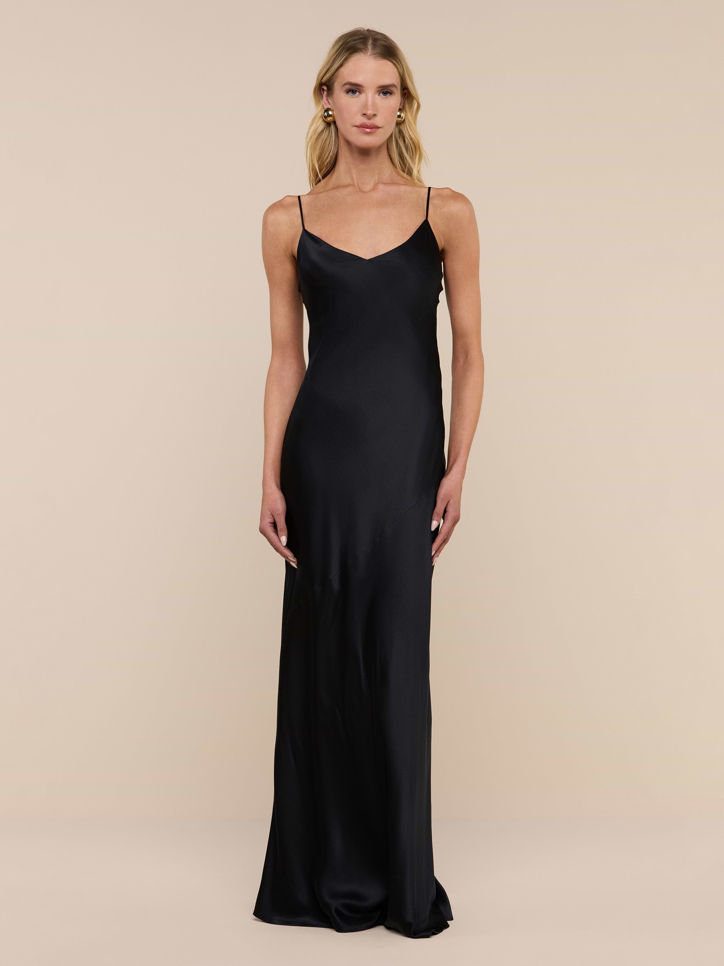 A woman stands against a plain white background wearing the Serita Silk Gown—a long, sleeveless black dress with thin straps, crafted from luxurious silk charmeuse.