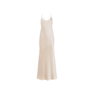 The Serita Silk Gown is a long, light champagne slip dress crafted from luxurious silk charmeuse, featuring thin spaghetti straps and a subtle flare at the hem, displayed on a white background.