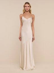 A woman stands against a plain white background, wearing the Serita Silk Gown—a long, sleeveless charmeuse slip dress in a champagne hue with thin straps.