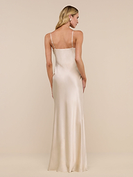 A woman with long blonde hair wears the floor-length Serita Silk Gown in light champagne, featuring thin straps, as she stands facing away against a plain white background.