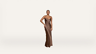 A person stands on a white background wearing a long, sleeveless, bronze satin dress, with one hand resting on their hip and a neutral expression.
