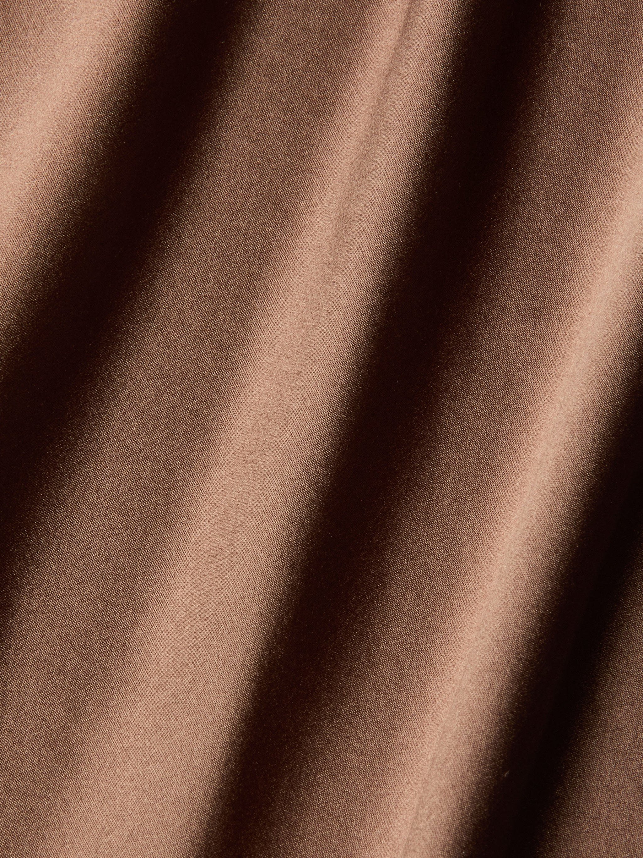 Close-up of the Serita Silk Gown, showcasing its brown silk fabric with soft diagonal folds and a lustrous, light-reflecting finish—an elegant choice for wedding guests.
