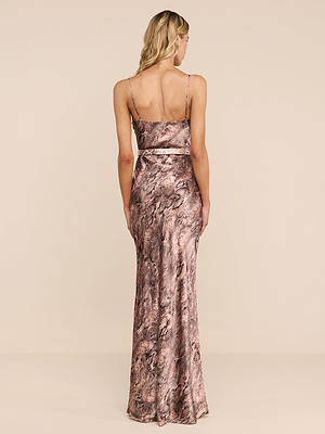 A woman with long blonde hair models the Serita Silk Gown—a sleeveless, floor-length marble-patterned slip dress with thin straps—shown from the back against a beige background; ideal as a chic wedding guest outfit.