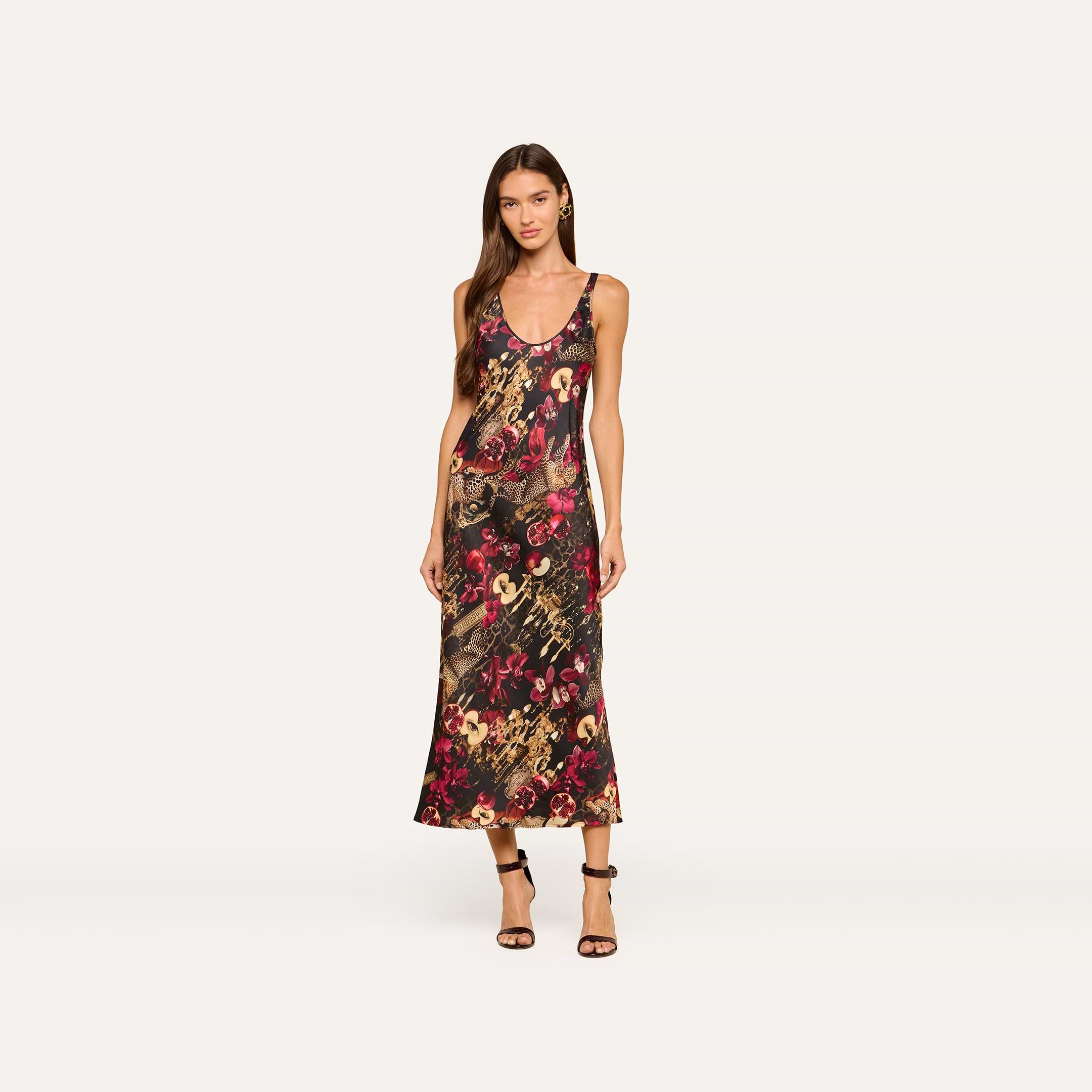A woman wearing the Akiya Satin Maxi Dress—a sleeveless, ankle-length tank dress featuring a colorful statement collage print—stands against a plain light background with black strappy heels.