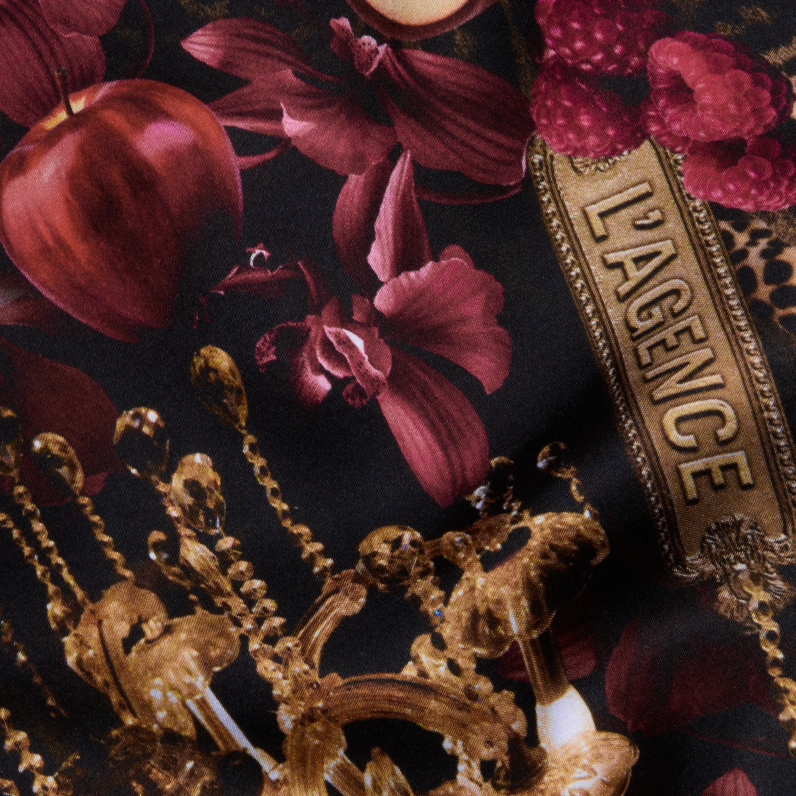 Introducing the Akiya Satin Maxi Dress, crafted from a statement collage print fabric adorned with red apples, orchids, gold chandeliers, raspberry clusters, and a gold-edged LAGENCE label set against a dark background.