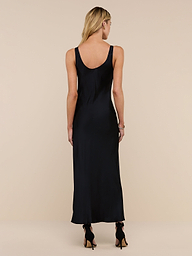 A woman with long blonde hair stands facing away against a plain white background, wearing the Akiya Satin Maxi Dress and beige heels.