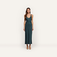 A woman wearing an Akiya Satin Maxi Dress in forest green, featuring a bias-cut, ankle-length scoop-neck style paired with tan pumps.