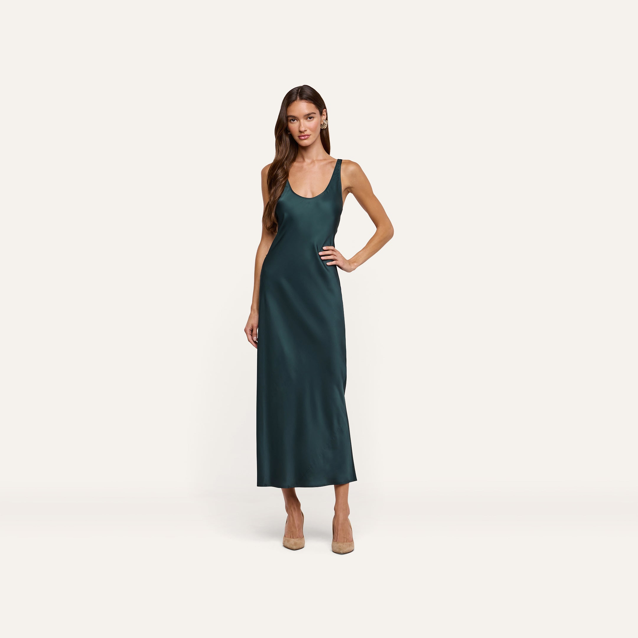 A person wears a forest green Akiya Satin Maxi Dress, a bias-cut style with a scoop neck, paired with tan heels.