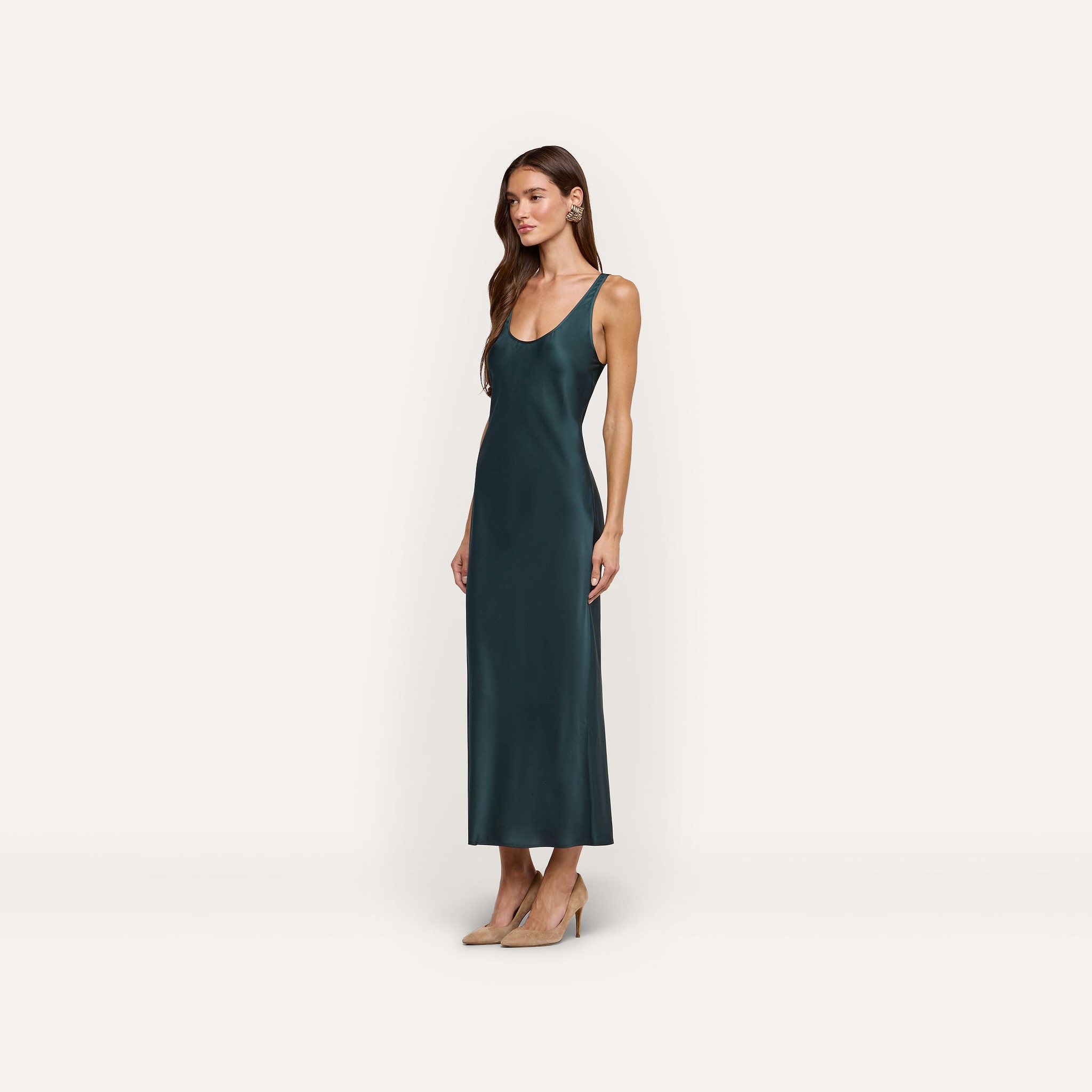 A woman wearing a sleeveless, floor-length forest green Akiya Satin Maxi Dress in bias-cut satin with tan high heels.