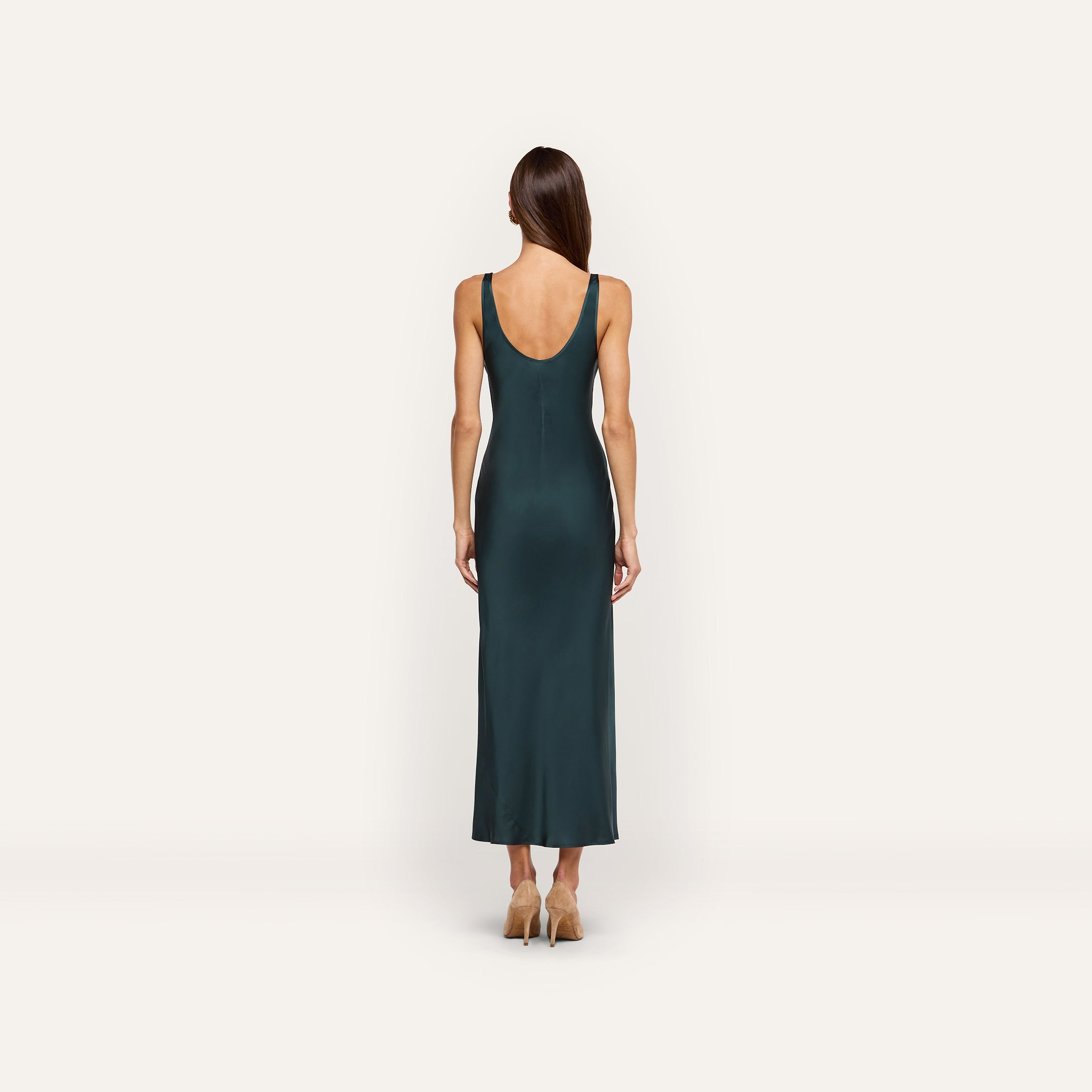 Back view of a person wearing the forest green, bias-cut satin Akiya Satin Maxi Dress with a scoop back and tan heels.