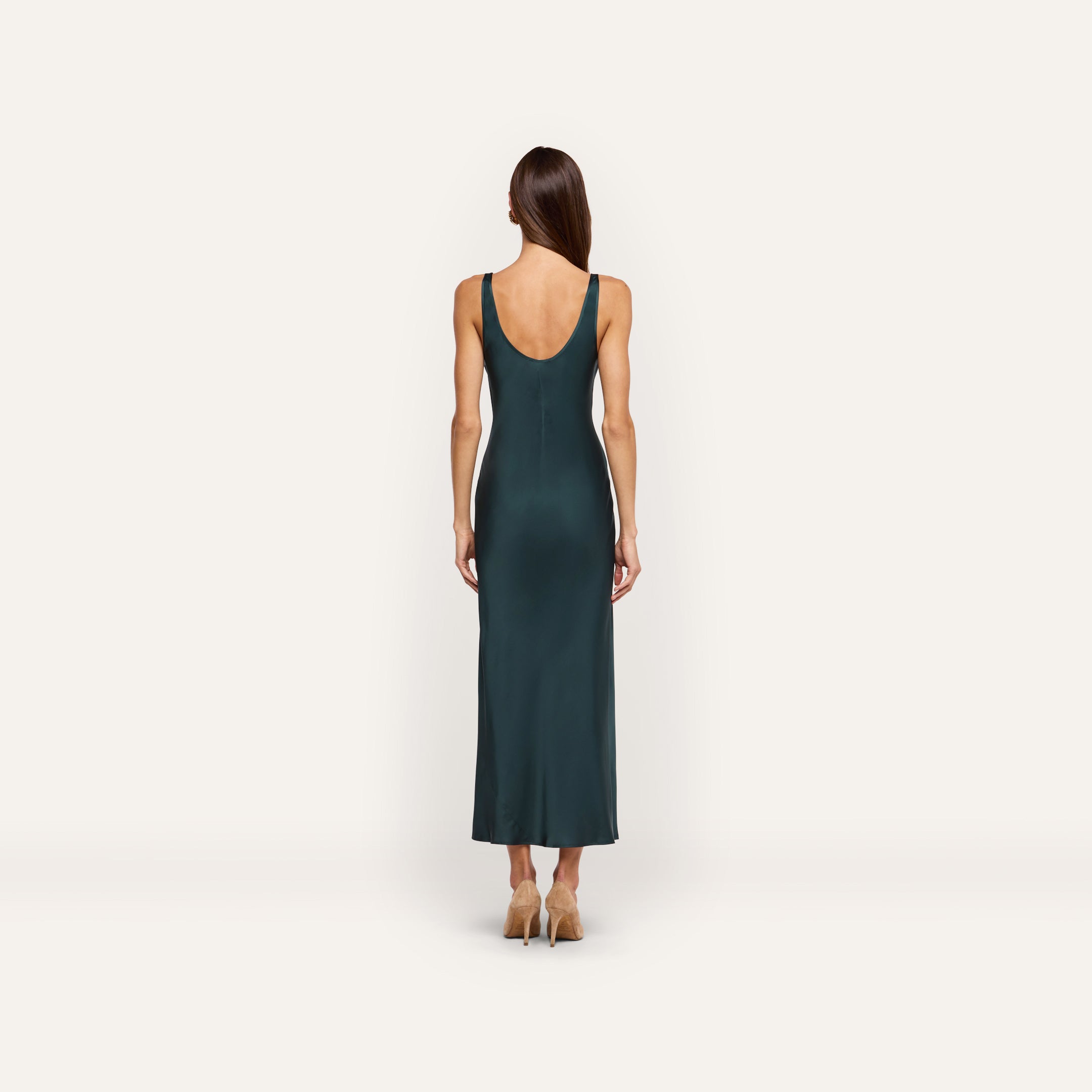 Back view of a person wearing the forest green, bias-cut satin Akiya Satin Maxi Dress with a scoop back and tan heels.