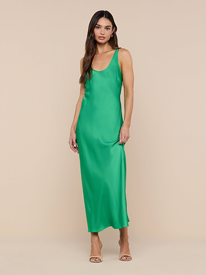 A woman stands against a beige background wearing the Akiya Satin Maxi Dress in island green, paired with nude open-toe heels. Her long hair is worn loose and she has a relaxed expression.