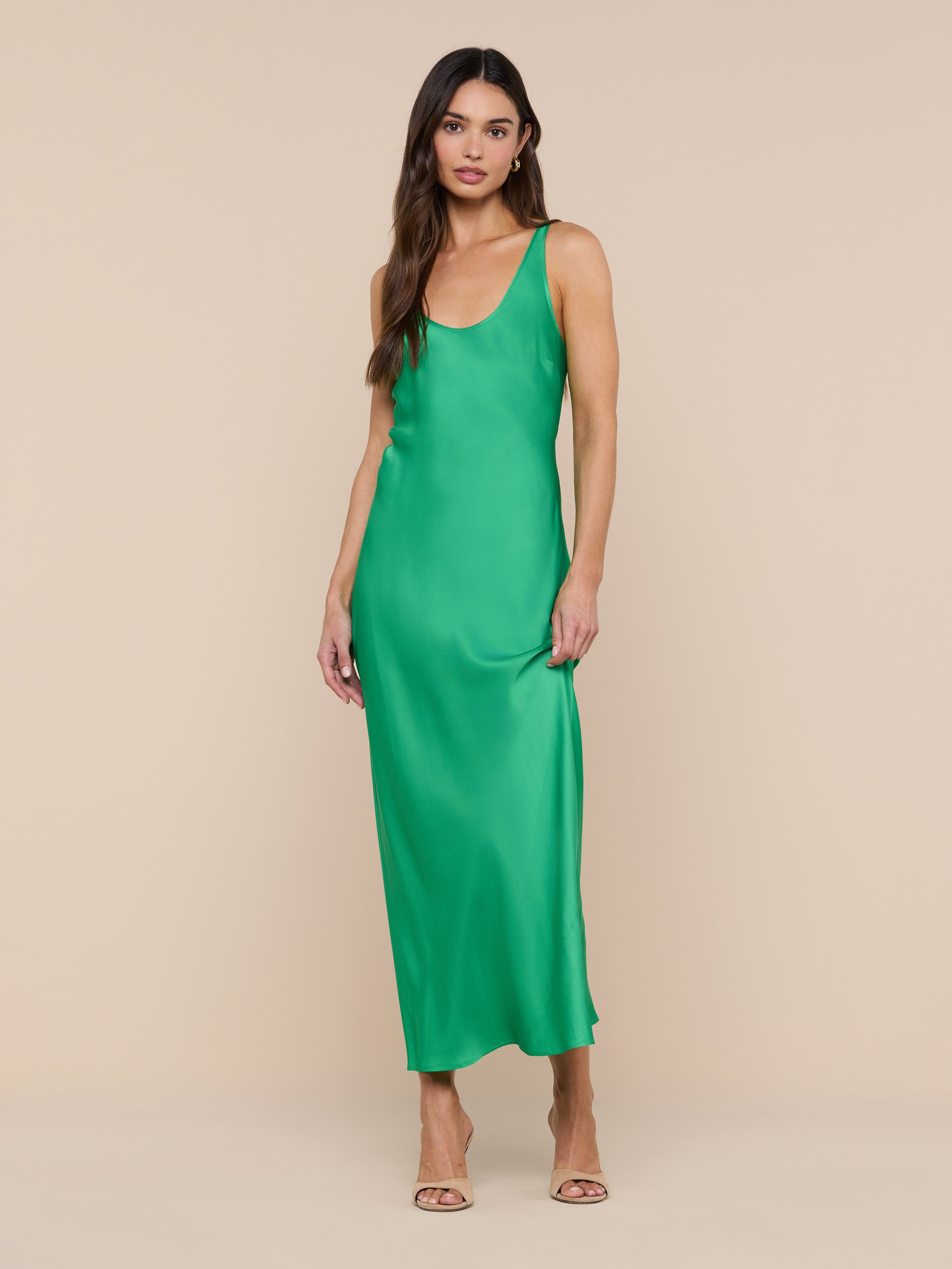 A woman stands against a white background wearing the Akiya Satin Maxi Dress in a sleeveless, island green bias-cut silhouette paired with open-toe heels.
