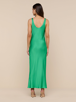 A woman with long brown hair faces away, wearing the sleeveless, island green Akiya Satin Maxi Dress with a low scoop back and nude heels against a beige background.