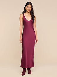 A woman stands against a plain white background, wearing the Akiya Satin Maxi Dress—a sleeveless, floor-length gown in deep burgundy—paired with matching burgundy boots.