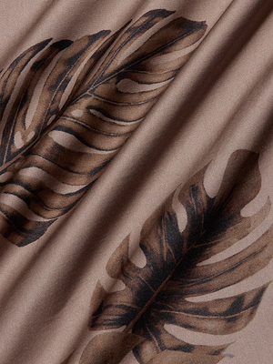 A close-up of light brown satin with a smooth texture and brown palm leaf print, detailed veins, and shading. The softly draped fabric is featured on the Akiya Satin Maxi Dress, creating gentle folds ideal for bias-cut styles.