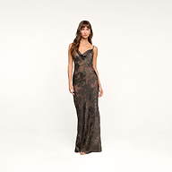 A woman stands against a plain background wearing the Christine Burnout Satin Gown—a long, fitted black dress with thin straps and a subtle floral pattern, reminiscent of a sheer slip dress.
