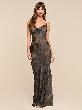 A woman wearing the Christine Burnout Satin Gown—a long, sheer black lace bias-cut dress with spaghetti straps—stands against a plain beige background.