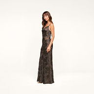 A woman in the Christine Burnout Satin Gown stands against a plain white background, facing slightly to the side with a neutral expression. Her elegant look evokes the essence of a sheer slip dress style.