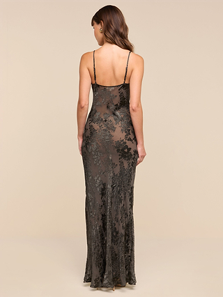 A woman stands with her back to the camera against a plain beige background, wearing the Christine Burnout Satin Gown—a long, sleeveless black dress with floral patterns and thin straps.