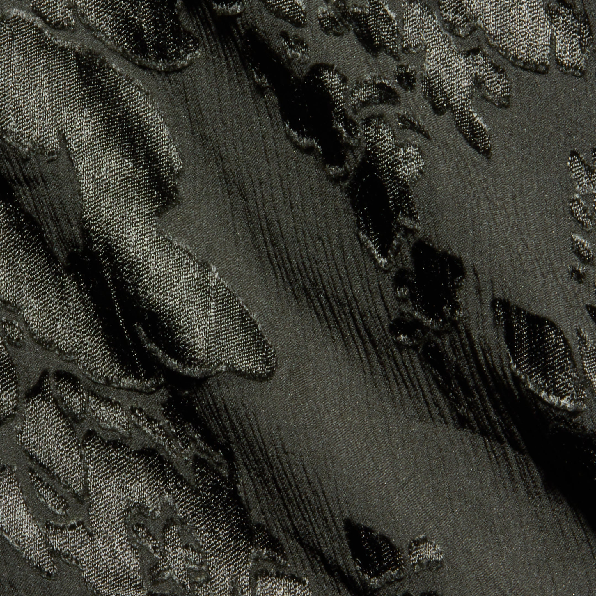 Close-up of textured dark fabric with raised, shiny floral or leaf patterns and a subtle sheen. The material features an embossed or jacquard weave design, similar to those found in the Christine Burnout Satin Gown.