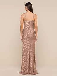 A woman with long brown hair stands facing away against a neutral background, wearing the Christine Burnout Satin Gown—a long, fitted, sleeveless dress in rose-gold featuring a textured geometric pattern.