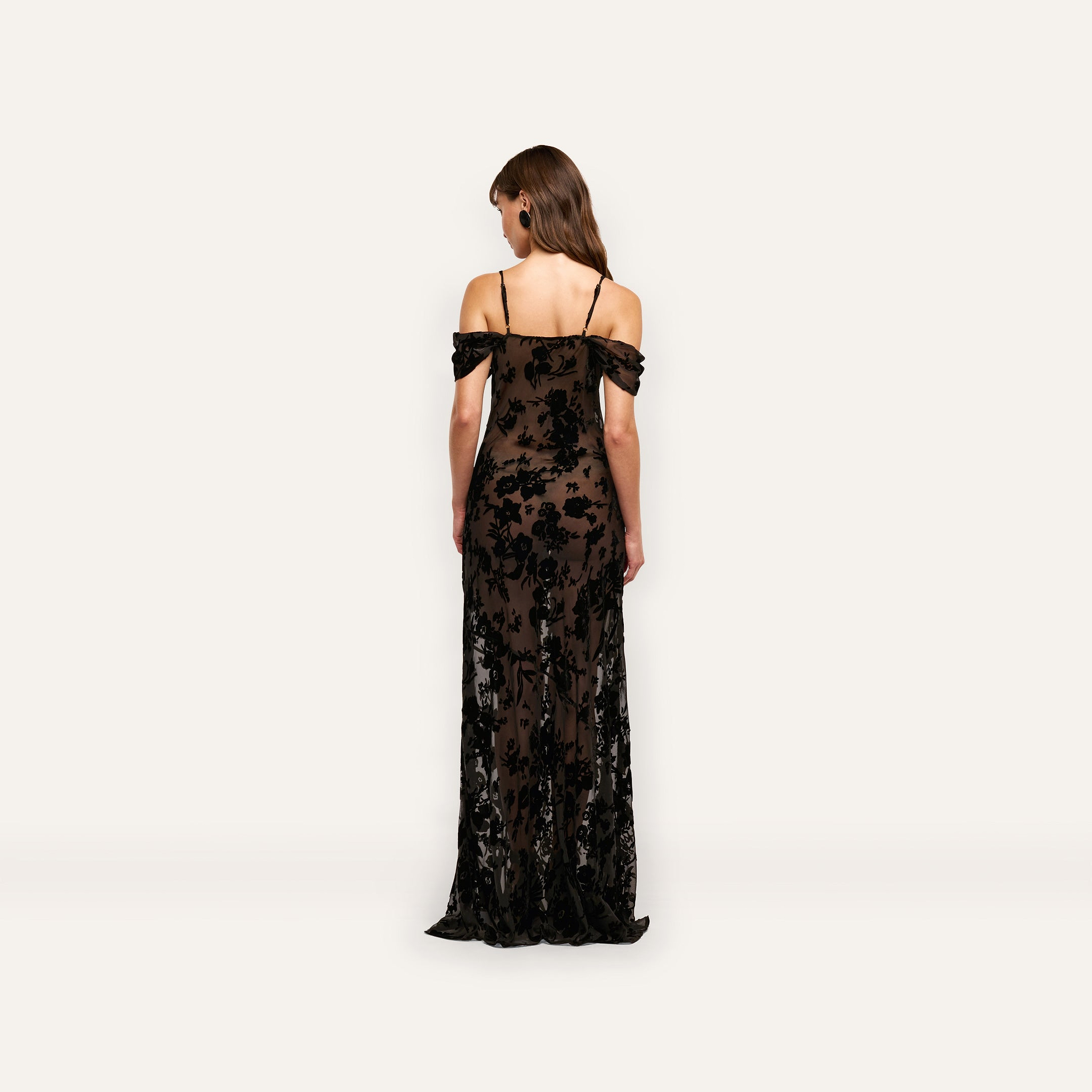Back view of the Kenna Velvet Gown, a floor-length, off-the-shoulder burnout velvet dress with thin straps and a black floral pattern over a dark base.
