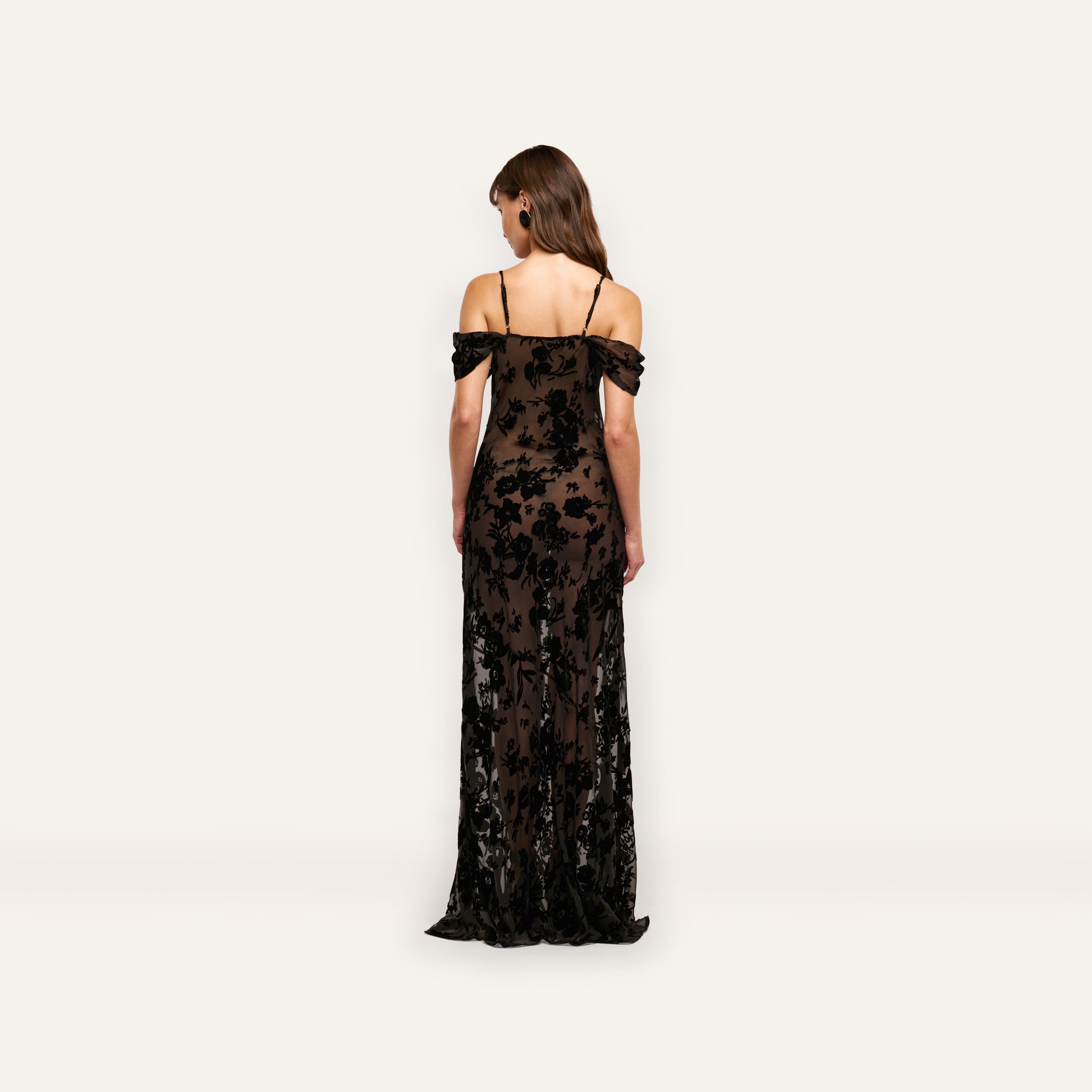 Back view of the Kenna Velvet Gown, a floor-length, off-the-shoulder burnout velvet dress with thin straps and a black floral pattern over a dark base.
