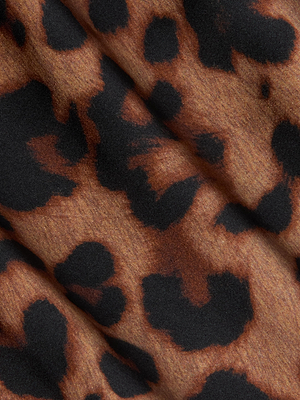 Close-up of the Seridie Silk Slip Dress by L'AGENCE, showing its leopard print with irregular black and dark brown spots on a light brown background. The softly folded silk highlights a smooth texture and subtle shadows.