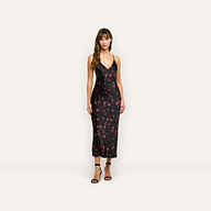 A woman wearing a black Seridie Silk Slip Dress in silk charmeuse with a red cherry print and black strappy high heels.