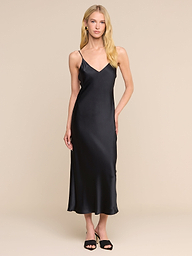 A woman with long blonde hair wears the Seridie Silk Slip Dress—a sleeveless, V-neck black design—paired with black heels, standing against a plain white background.
