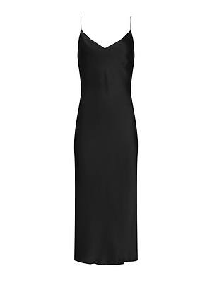 A woman with long brown hair stands in a minimal room, facing away from the camera, wearing the Seridie Silk Slip Dress— a black, sleeveless, backless midi slip dress with thin straps—paired with black high-heeled shoes.