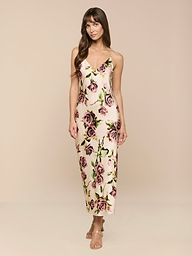 Una mujer con el pelo largo y castaño lleva el vestido Seridie Silk Slip Dress -un slip de seda cortado al bies, largo hasta los tobillos y con un estampado de rosas rosas y verdes- combinado con sandalias de tiras, sobre un fondo beige claro.