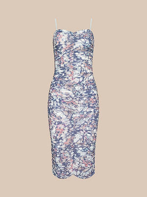 The Caprice Midi Dress is a knee-length bodycon with thin adjustable straps and multicolored abstract floral patterns inspired by butterfly wings, set against a light background on a plain beige backdrop.