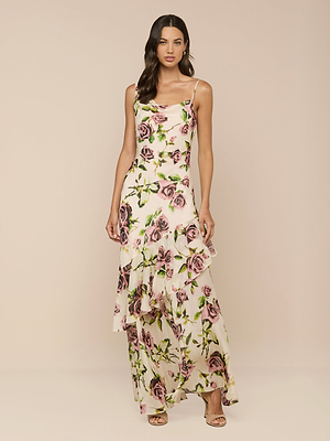 Una donna con lunghi capelli castani ondulati indossa labito Viola Silk Cowl-Neck Gown, caratterizzato da un design senza maniche, stampa di rose color malva, orlo increspato e spalline sottili. Lo abbina a tacchi aperti beige su uno sfondo neutro.