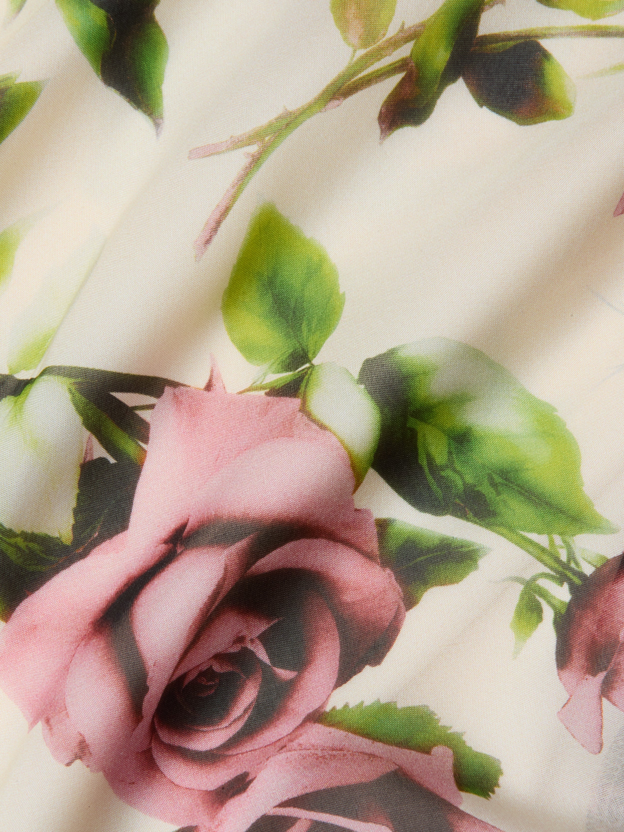 A close-up of silk chiffon with a mauve rose and green leaf print on a creamy backdrop, ideal for crafting the romantic Viola Silk Cowl-Neck Gown.