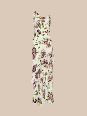 Labito Viola Silk Cowl-Neck Gown è un abito midi senza maniche in chiffon di seta bianco con stampa di rose color malva, scollo a cappuccio e orlo asimmetrico con volant, su sfondo beige.