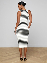 A woman wearing the Nura Racerback Midi Dress, a black-and-white striped, sleeveless, fitted midi dress with a racerback silhouette, stands facing away in black heels, her hair styled in a bun.