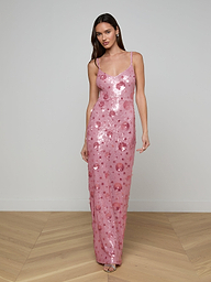 A woman wearing the Karma Sequin Maxi Dress—a long, pink gown with spaghetti straps—stands against a plain, light background.