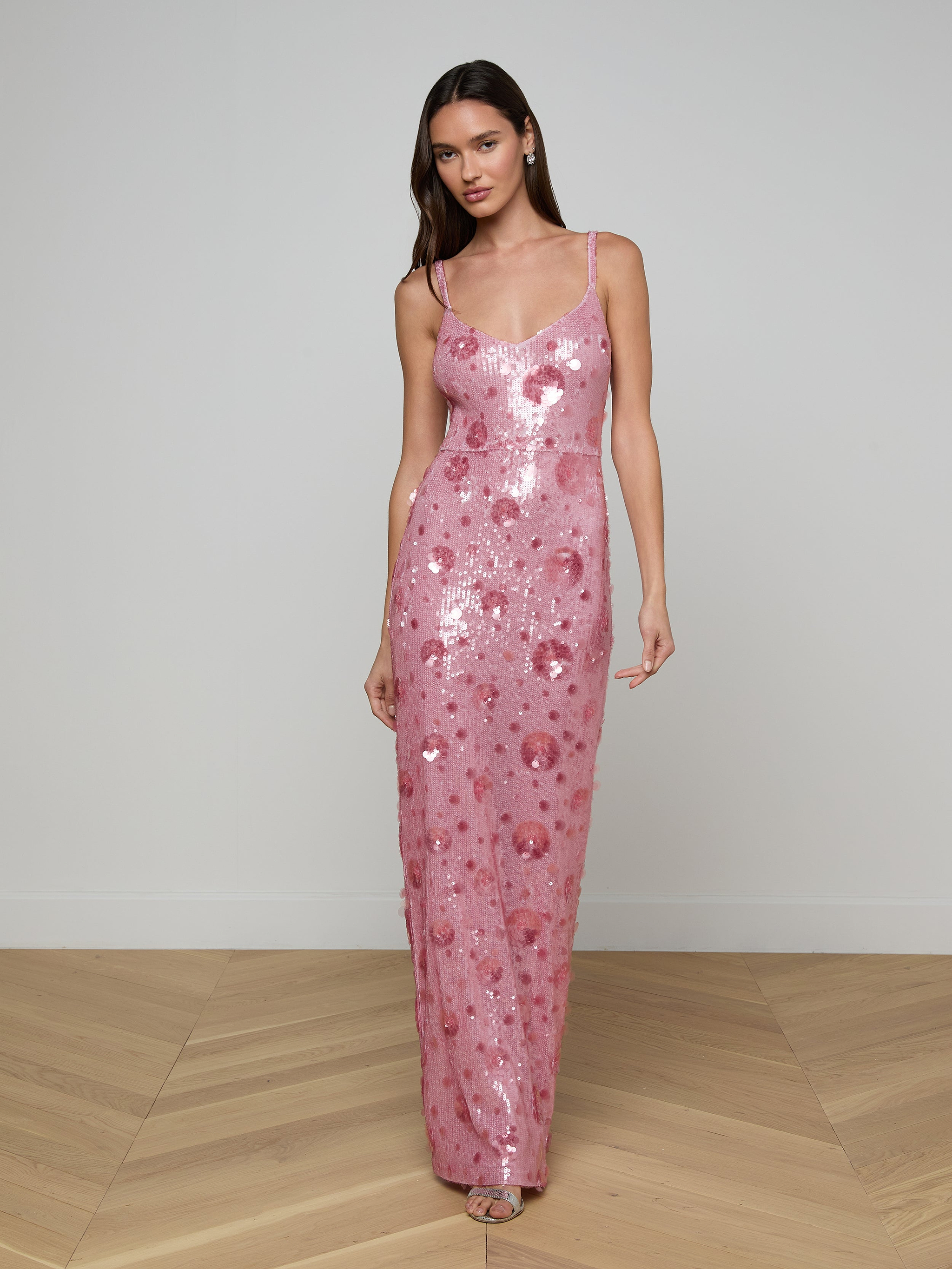 A woman wearing the Karma Sequin Maxi Dress—a long, pink gown with spaghetti straps—stands against a plain, light background.