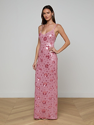 A woman wearing the Karma Sequin Maxi Dress—a sleeveless, floor-length gown with a fitted silhouette, spaghetti straps, and large pink sequin embellishments featuring subtle floral patterns—stands against a plain white background.
