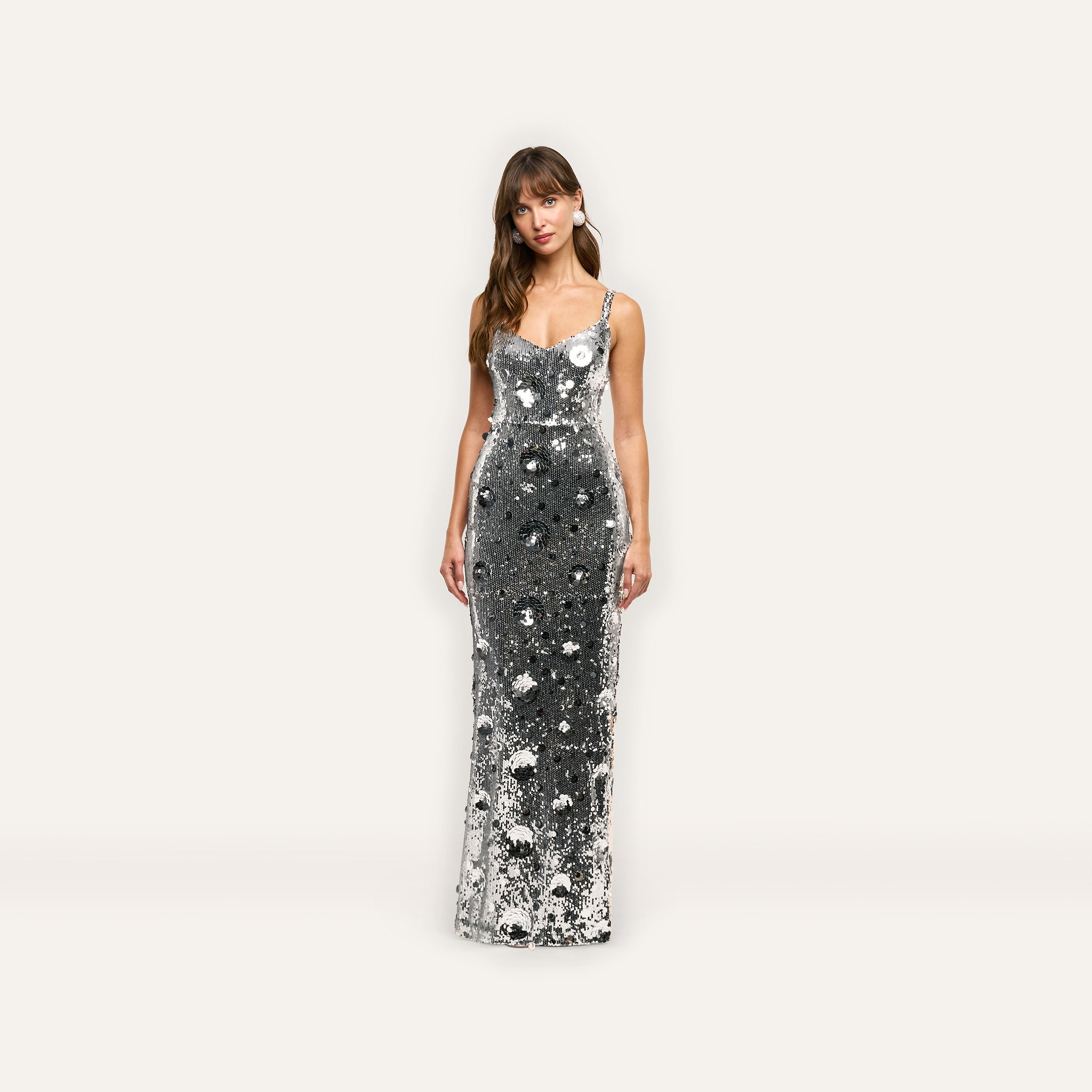 A person wearing a floor-length, sleeveless silver sequin Karma Sequin Maxi Dress adorned with a floral pattern.