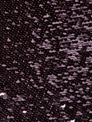 Close-up of the Karma Sequin Maxi Dress by L'AGENCE shows its surface covered in small, shiny dark purple sequins. The overlapping sequins reflect light for a shimmering, textured effect.
