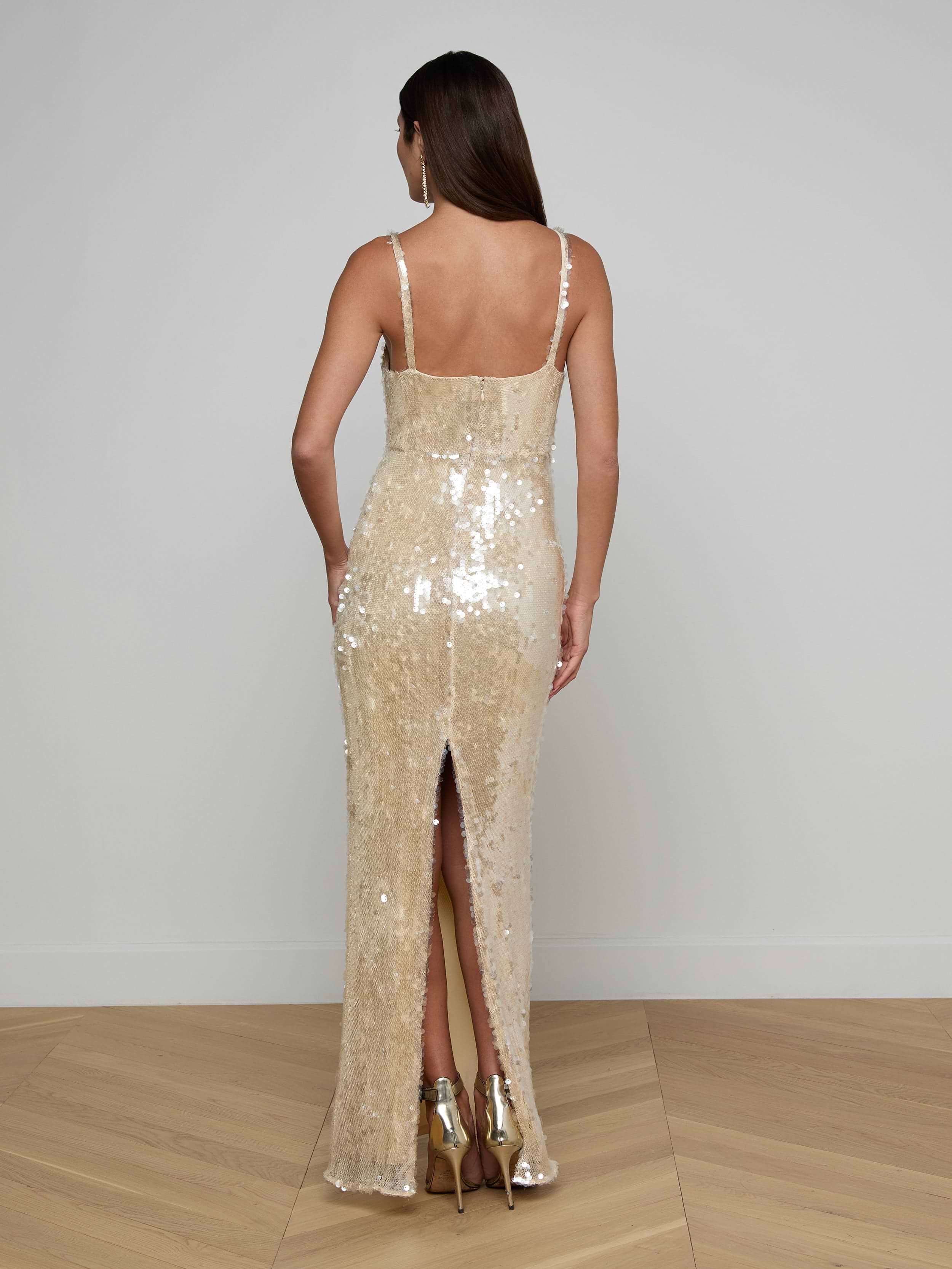 A woman with long brown hair is pictured from behind against a plain white background, wearing the sleeveless, backless Karma Sequin Maxi Dress featuring a back slit.