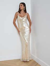 A woman wearing the Karma Sequin Maxi Dress—a sleeveless, floor-length gold dress featuring shimmering sequins and a V-neckline—stands against a plain white background. This elegant gown is perfect for NYFW 2026.