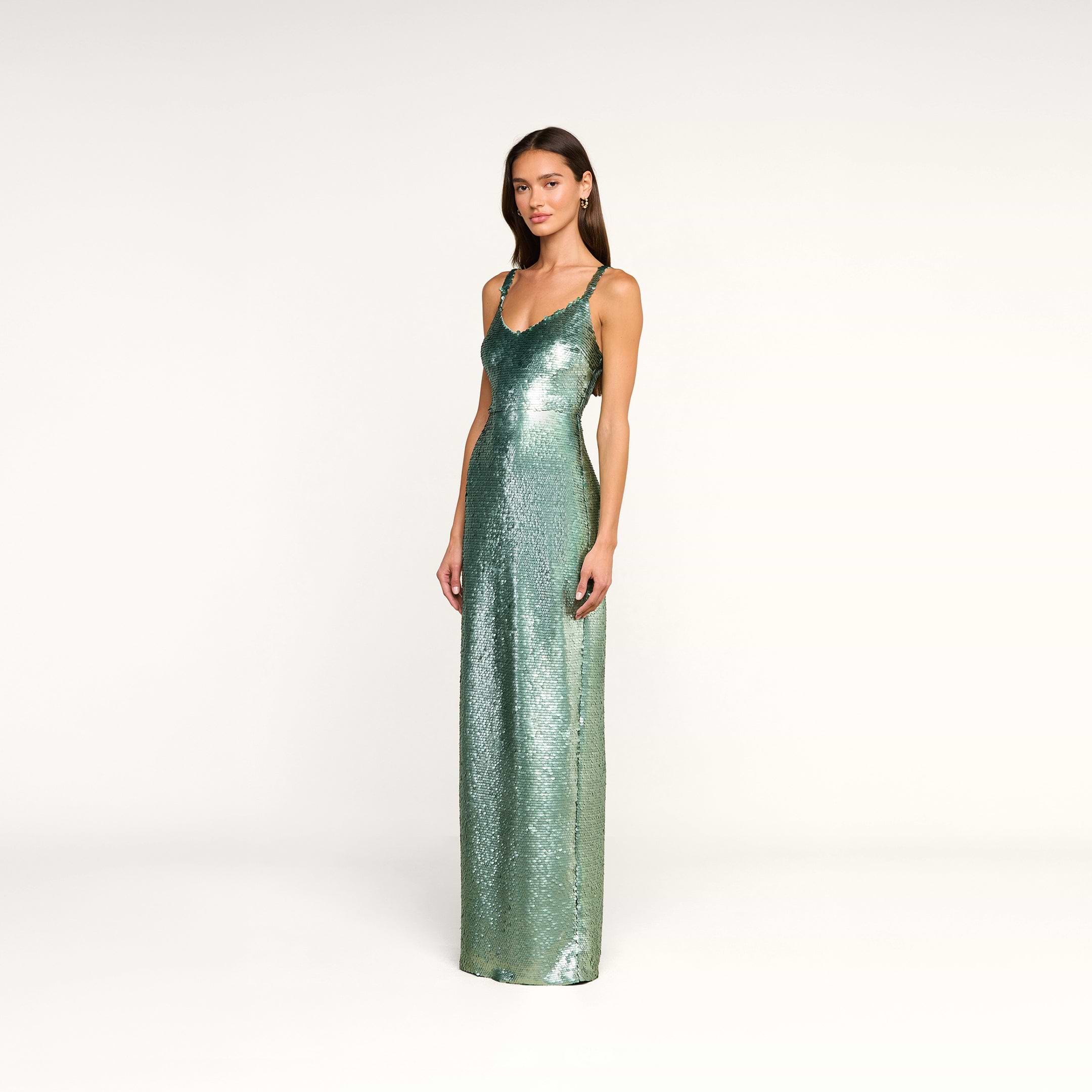 A woman stands in the Karma Sequin Maxi Dress—a fitted teal maxi dress with thin straps—posing against a plain white background.