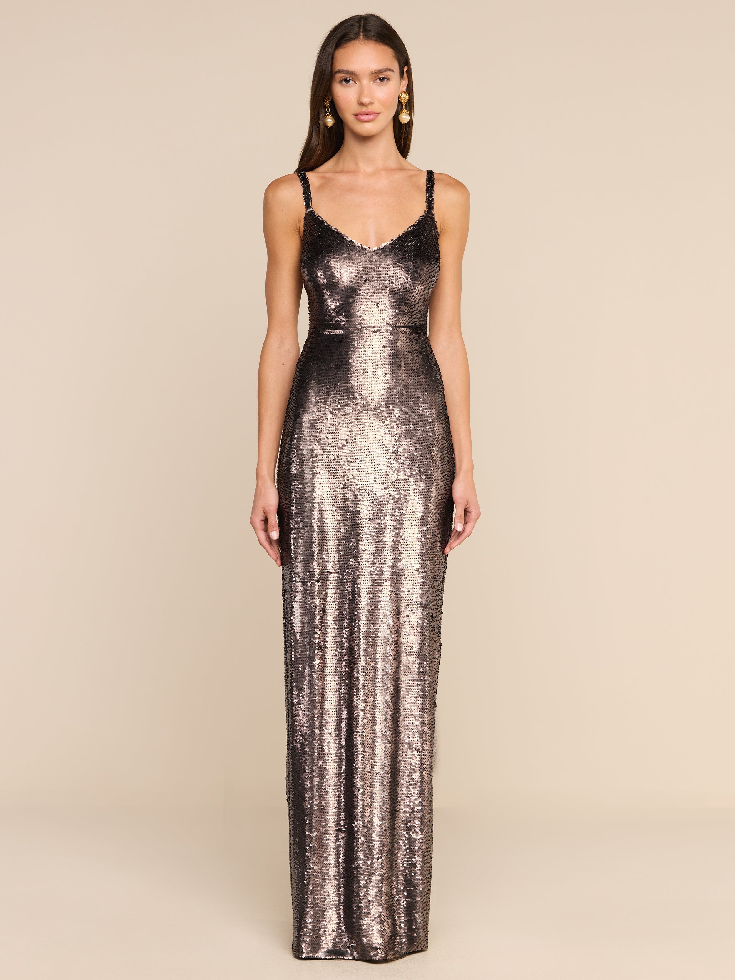 A woman stands facing forward wearing the Karma Sequin Maxi Dress, a long, fitted dress with thin straps covered in sequins. The background is plain white.