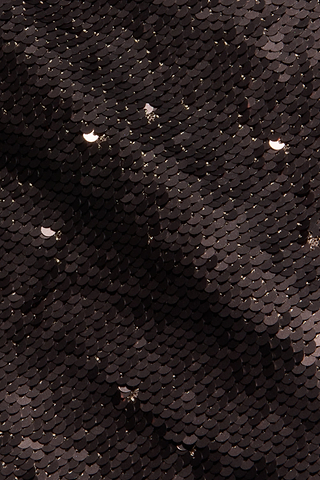 Close-up of densely layered, small black sequins on the fitted Karma Sequin Maxi Dress, with a few reflecting light to create a textured, shimmering surface.